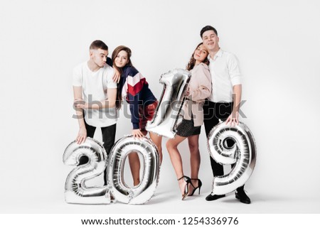 Group of happy friends of two girls and two guys dressed in stylish clothes are holding balloons in the shape of numbers 2019 on a white background in the studio