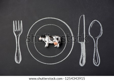 Toy white and black cow on a plate in the figure on the chalk board
