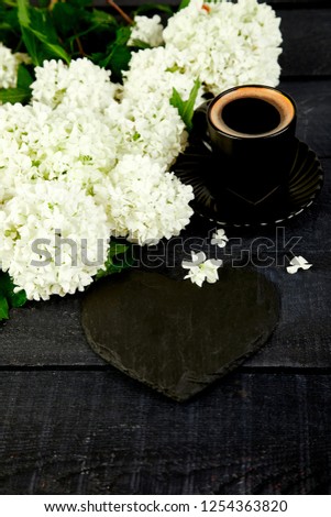 Cup of coffee with bouquet flower hydrangea and slate heart on black wooden background. Good morning. Flat lay. Top view. Love.
