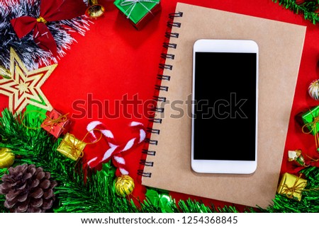 Top view image of Christmas festive decorations with empty smartphone,notebook and pencil on red paper background, New Year concept.