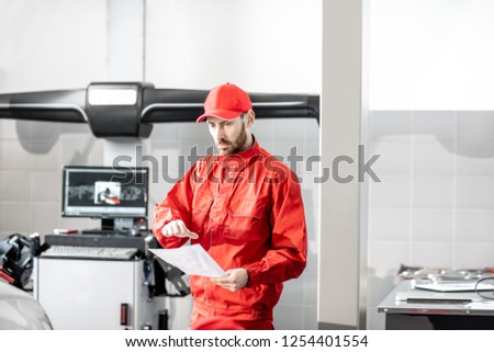 Auto mechanic in red uniform working with computer doing wheel allignment at the car service