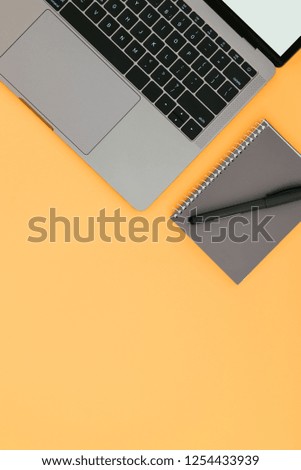Gray laptop and notepad with pen isolated on an orange background, flatlay, copyspace.