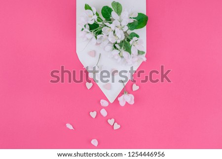 Creative flat lay concept top view of blank letter envelope and apple tree flowers on millennial pink background with copy space in minimal style, template for celebration, invitation, valentine cards