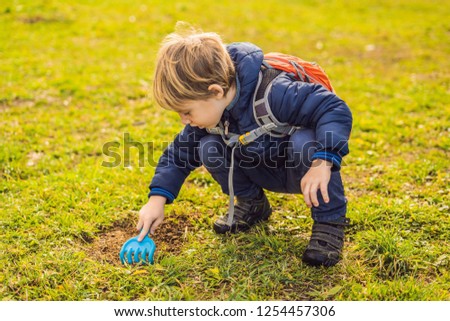 The boy plays recycling. He buries plastic disposable dishes and biodegradable dishes. After a few months, he dug up the dishes and saw that the biodegradable dishes began to decompose and plastic did