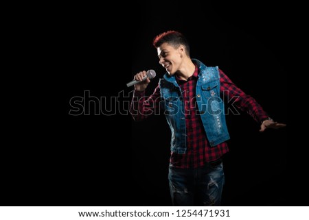 Woman singer with red hair in a denim suit with a microphone in her hand sings in the studio on a black background