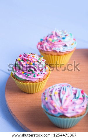 Closeup different colorful cupcakes decorated with sprinkles on wooden round desk. Multicolored pastel desserts.