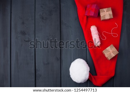 Red Cap with Pompon Santa Claus. On a black wooden background, gifts and Christmas decor. Free space for text. Top view