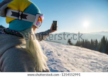 Woman snowboarder relaxing after snowboarding, taking photos of winter nature in the mountains using smart phone in the morning copyspace connectivity mobility carrier lifestyle technology