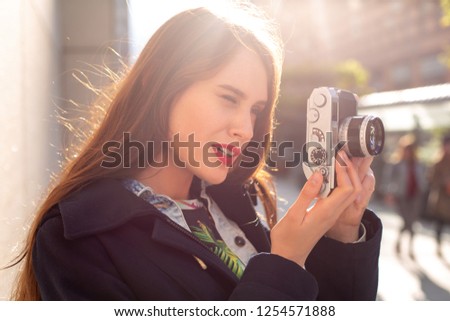 Outdoor autumn smiling lifestyle portrait of pretty young woman, having fun in the city with camera, travel photo of photographer.