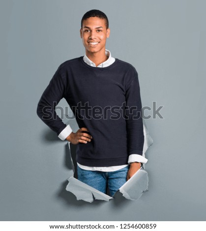 Young african american man posing with arms at hip and laughing looking to the front through a paper hole