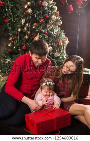 beautiful young family with a small daughter are sitting near a New Year tree with gifts on a holiday