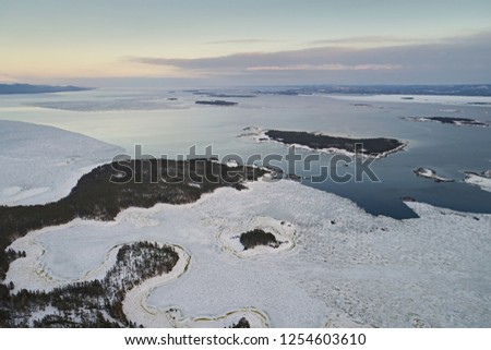Aerial view of the archipelago and the sea, with a partially frozen water surface against the sky in the evening. Winter landscape with the islands of the northern country with drone.