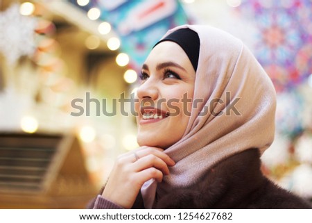 An adorable, smiling, Muslim girl in a rose hijab in the department store in the Christmas Eve in Moscow Royalty-Free Stock Photo #1254627682