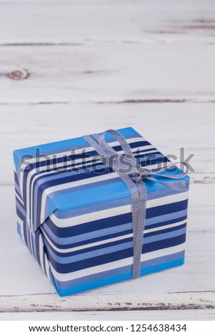 Beautiful gift box with copy space. Blue striped present box tied with silver ribbon. Holiday greeting background.