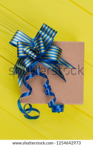 Kraft box with blue striped ribbon. Top view. Yellow wood background.