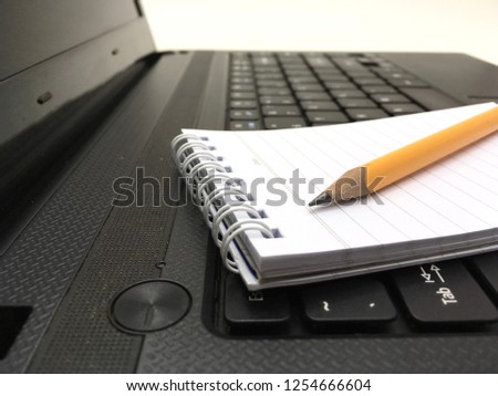 Closeup image of note pad and pencil on laptop keyboard