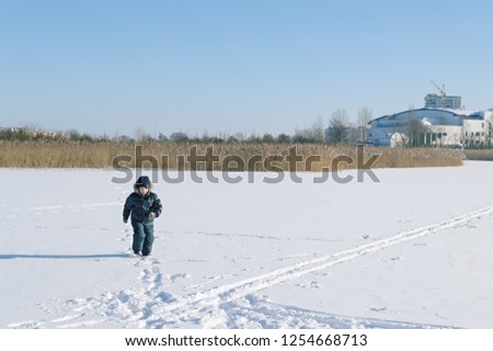 A boy in a frosty sunny winter day runs along a snowy field crossing the ski track