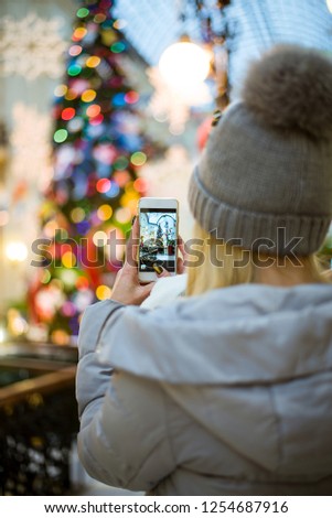 the girl in winter clothes make photo of the Christmas tree on the phone, a girl is taking pictures of Christmas tree on the phone (vertically, cold toned, close up)