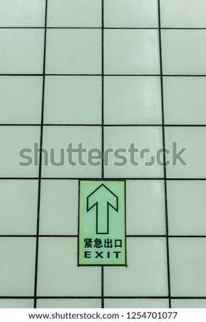 Dark Green Colored Arrow Sign in English and Chinese on the Tiles Floor