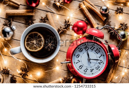Christmas cup of tea and alarm clock near fairy ligths around on wooden background
