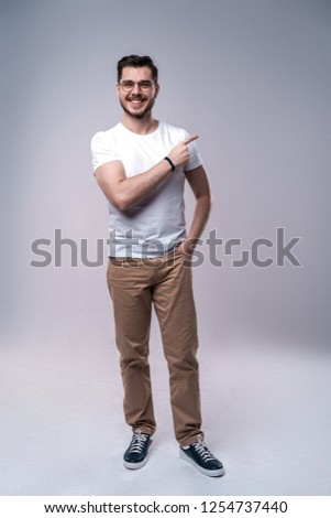 smiling young casual man presenting something on gray background