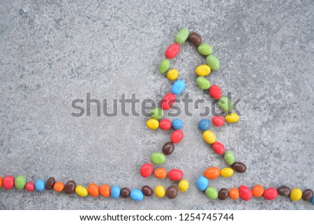 on a stone surface lie chocolate beans that give the outline of a Christmas tree - different colored chocolate coins lie in the shape of a Christmas tree on a stone surface