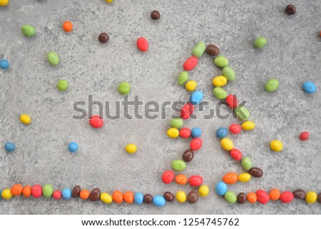 on a stone surface lie chocolate beans that give the outline of a Christmas tree - different colored chocolate coins lie in the shape of a Christmas tree on a stone surface