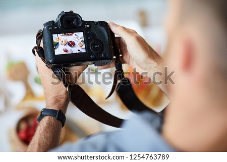 Above view closeup of unrecognizable photographer holding professional photo camera while taking pictures of food on table, copy space
