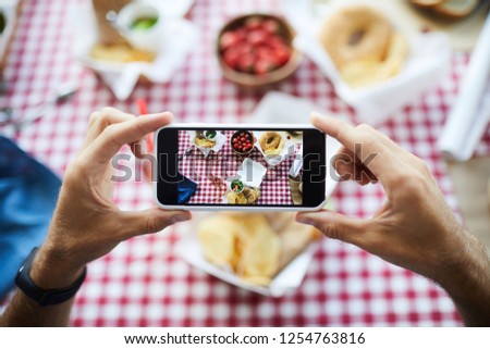 Top view closeup of unrecognizable man holding smartphone and taking pictures of food on picnic table, copy space
