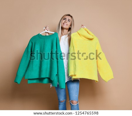 Woman shopping Christmas sale choose between two sweaters blouse green and yellow happy smiling on beige background
