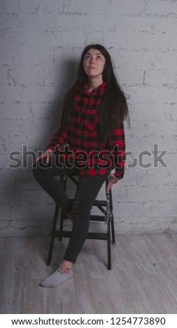 The girl in the red black plaid shirt. Brunette posing with a chair, against a brick wall. Beautiful woman on grey background. 