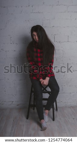 The girl in the red black plaid shirt. Brunette posing with a chair, against a brick wall. Beautiful woman on grey background. 