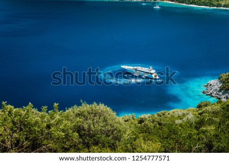 Luxury white yacht sail boat anchoring in a tranquil bay in deep blue water water, near picturesque shore of greek islands