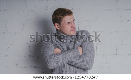 The guy in the warm sweater on the chair, on a gray background. A man posing against a brick wall.
