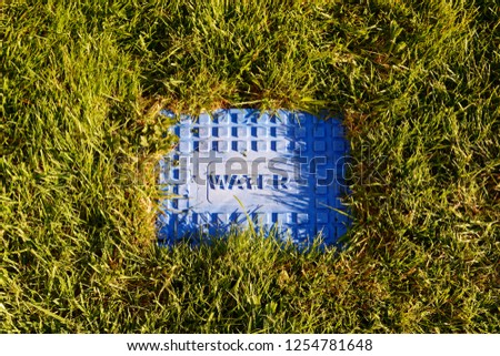A blue metal cover over a water station set in green grass