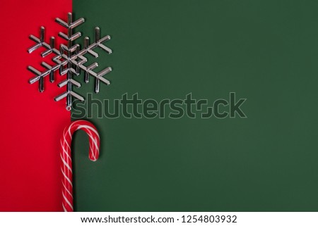 Christmas flatlay with candy canes and silver snowflake on the bright red and green background.