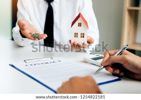 Customer writing signing signature on paper contract with real estate agent and giving key to client.