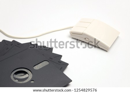 Retro white three-button computer mouse with five-inch floppy disks for storing information on a white background. Image of outdated computer technology and devices.