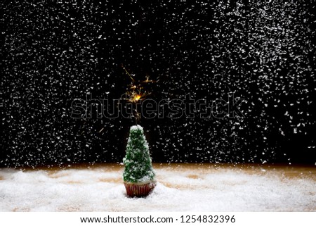 Little Christmas tree with burning sparkler on a black background with falling snow. Christmas concept.