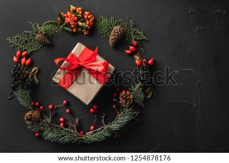 Crown of Christmas tree branches, pine cones, berries, walnuts, gifts, on black stone background. Xmas and Happy New Year theme. Flat lay, top view