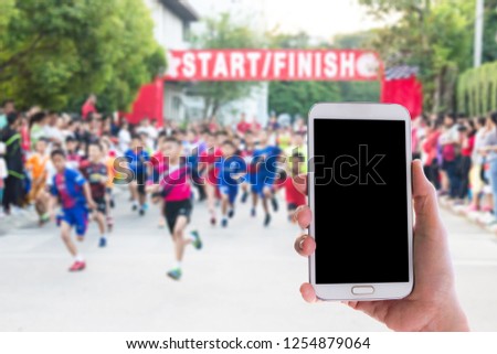 Man use mobile phone, blur image of running a mini marathon of children as background.