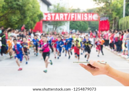 Man use mobile phone, blur image of running a mini marathon of children as background.