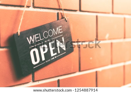 Open sign hanging on brown stone wall texture background. Business and service concept.