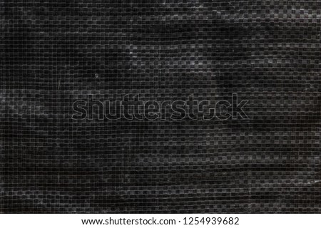 The texture of black polyethylene woven fabric. Abstract dark background of synthetic polypropylene or polyethylene (PP, PE) material which used as outdoor tarpaulin Royalty-Free Stock Photo #1254939682