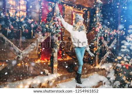 A pretty girl is on the porch in front of the house decorated for Christmas. Winter fashion for kids. Merry Christmas and Happy New Year.