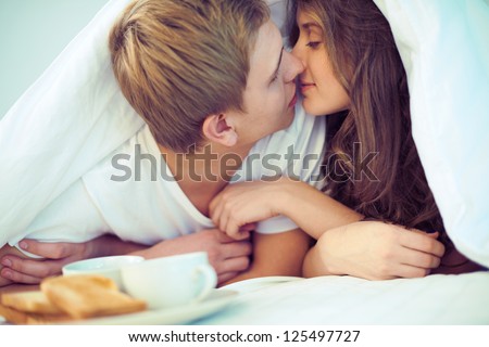 Young amorous couple kissing under blanket Royalty-Free Stock Photo #125497727