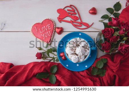 Romantic breakfast on valentine's day. Blue cup of hot beverage with biscuits and red roses on a white wooden table. Morning surprise for lovers. Top view.