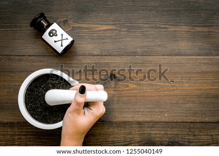 Prepare poison. Bottle with skull and crossbones near hand which make powder in mortar on dark wooden background top view copy space
