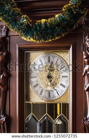 Vintage pendulum clock in a brown wooden carved case is decorated with Christmas garland close up
