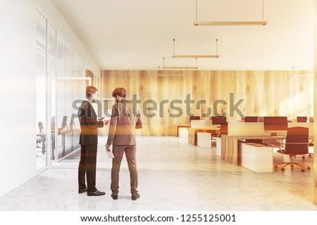 Businessmen in interior of modern office with white and wooden walls, concrete floor, white and wooden computer tables and black chairs. Toned image